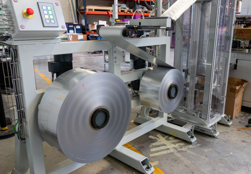 Industrial unwind system feeding roll materials into a PAKINA / MULTIPAK production line for composite can closing, sealing, and finishing operations.