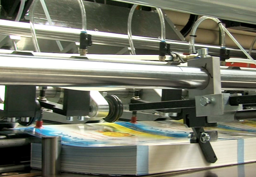 Bedruckte Etikettenbögen werden ausgerichtet und einer automatischen Rundetikettiermaschine für die hochwertige Dekoration von Verbunddosen zugeführt.
